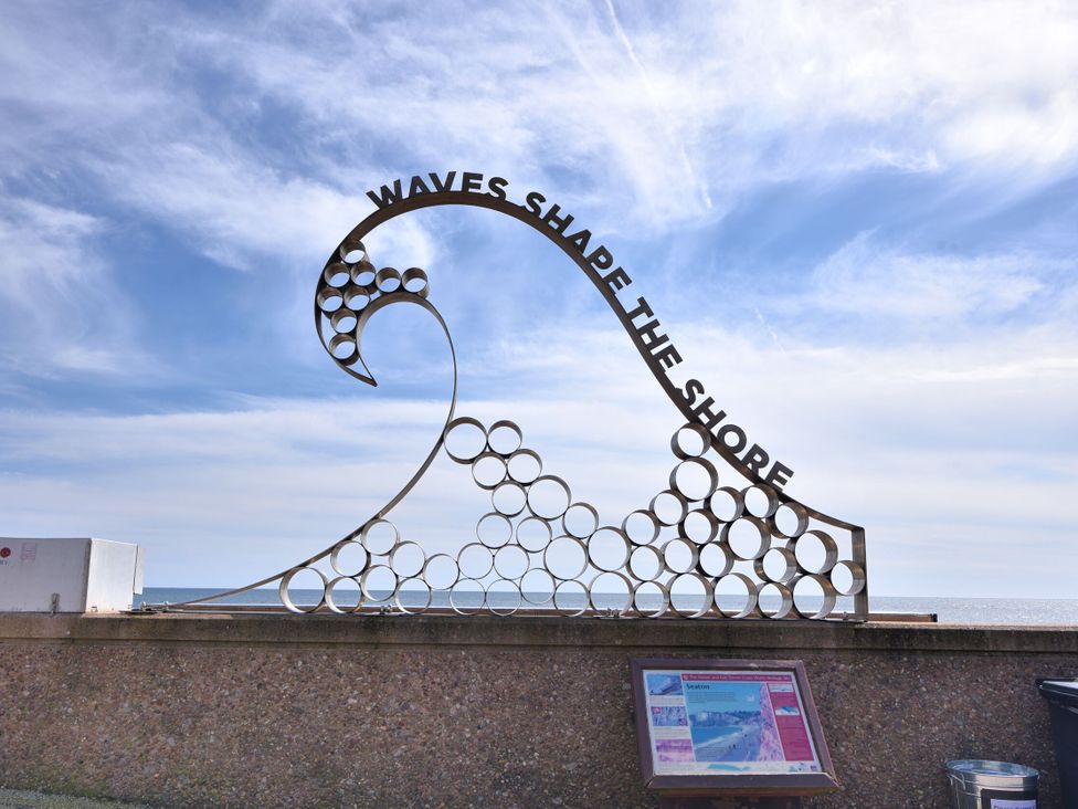 A metal sculpture of a wave with the words waves shape the shore by the seaside at Megs Roost in Shute near Colyton