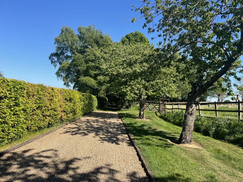 A gravel path lined with hedges and trees leading to a gate at Beechwood in Wood Norton near Foulsham