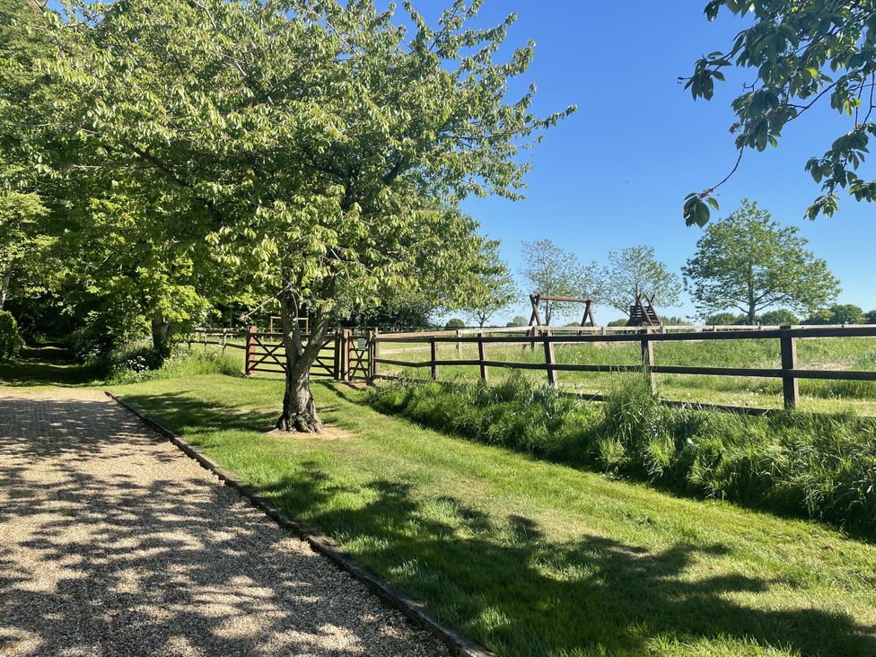 A garden with a path, trees, a swing set, and a fence at Beechwood in Wood Norton near Foulsham