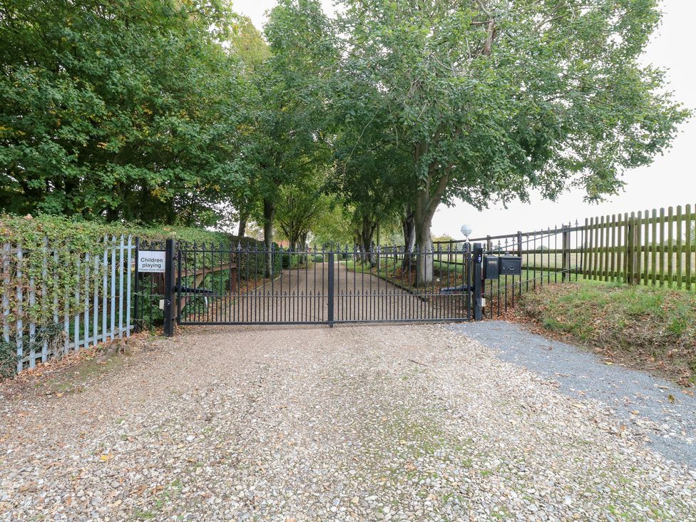 An entrance gate and gravel path surrounded by trees at Willow in Wood Norton near Foulsham