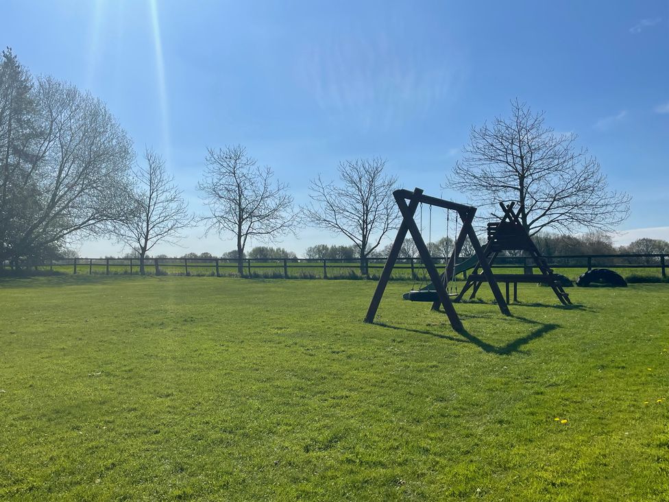 A play structure and swing set in a grassy area at Pear Tree Wood Norton