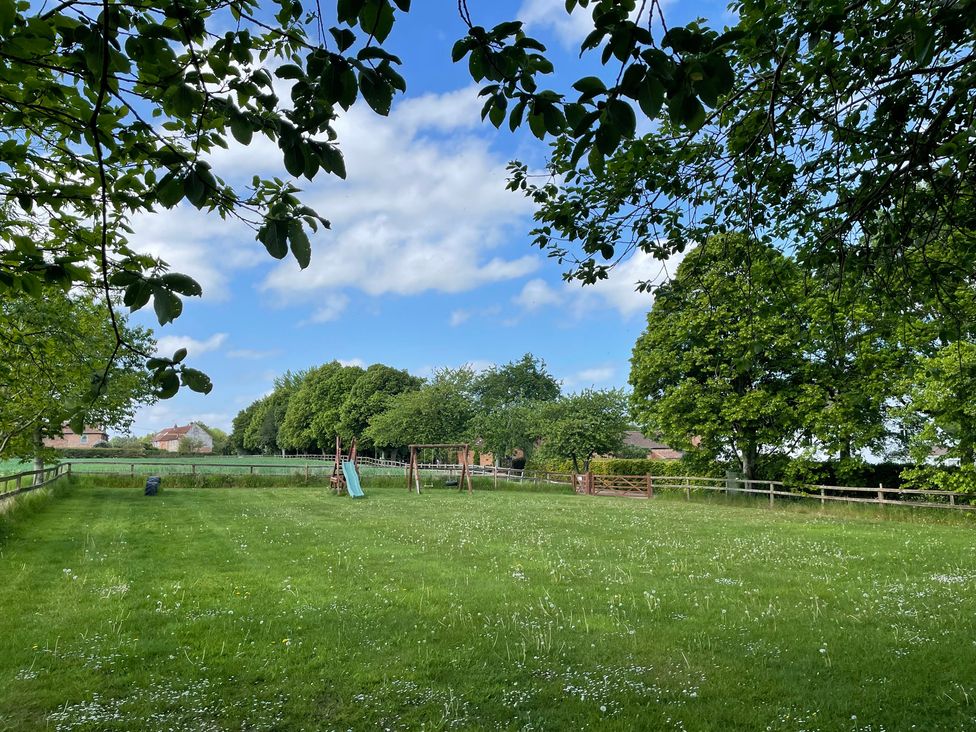 A garden with play equipment and trees at Pear Tree in Wood Norton