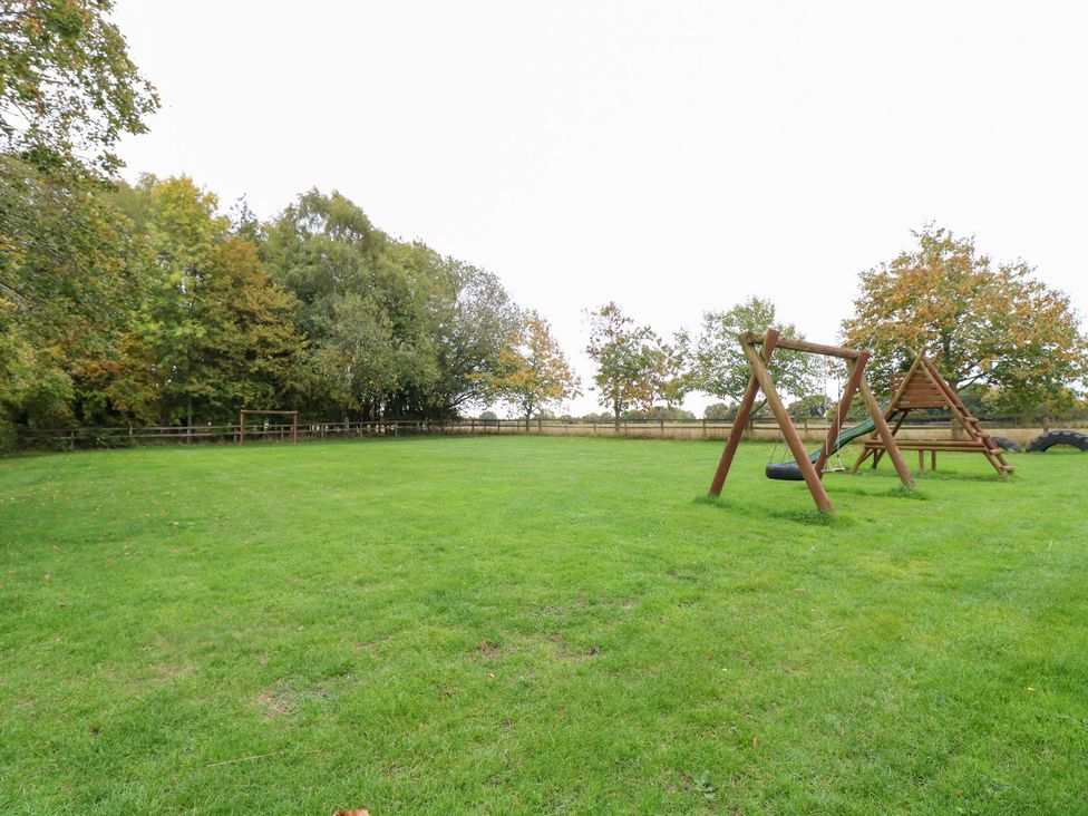 An outdoor area with a swing set and tire swing at Pear Tree in Wood Norton