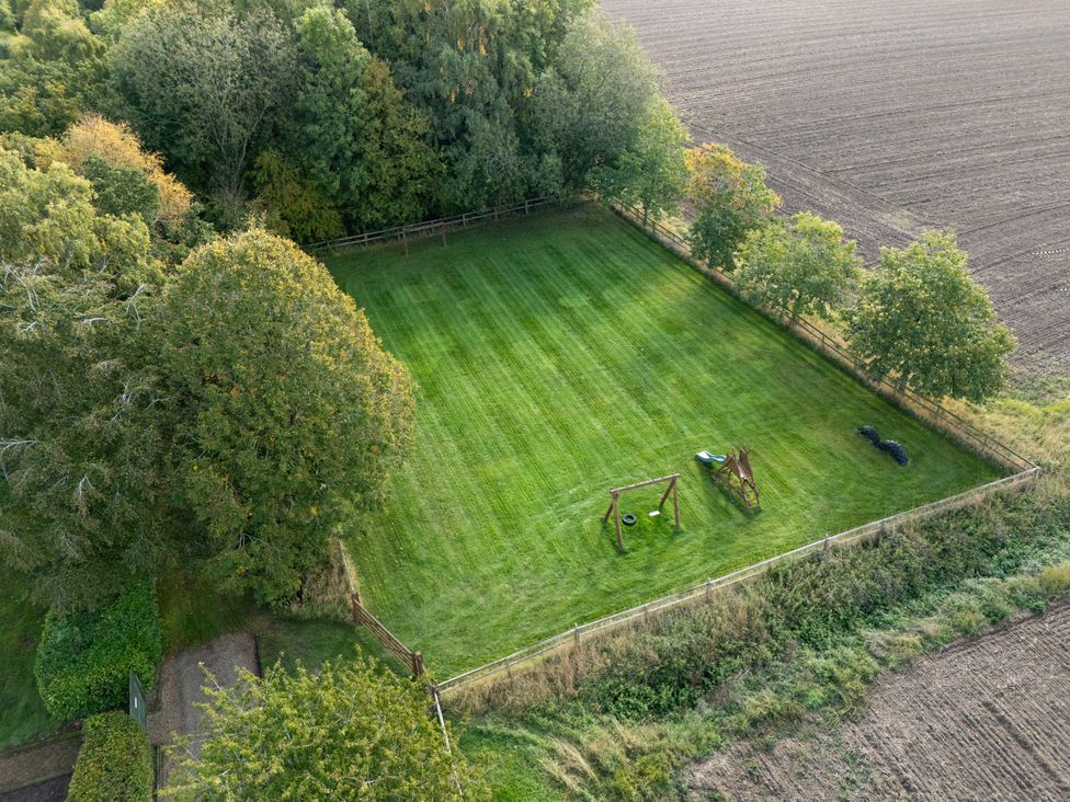 A grassy area with a swing set and trees at Holly Berry in Wood Norton near Foulsham