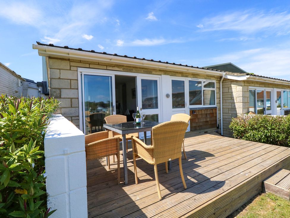 An outdoor wooden deck with a table and four wicker chairs outside a stone house at Cape 14 in Yarmouth