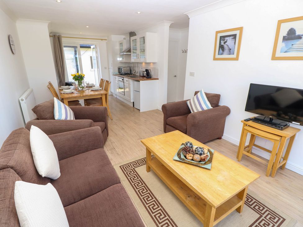 A living room with brown sofas a wooden coffee table a television on nested tables and a dining table near a kitchen at Cape 14 in Yarmouth