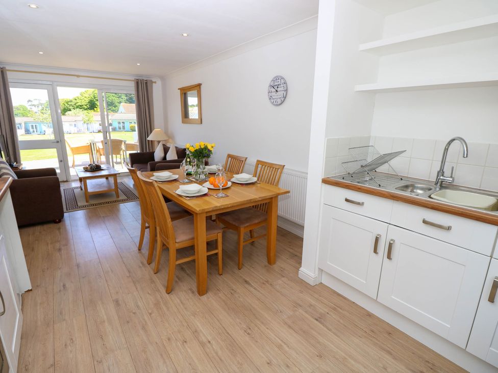 A kitchen and dining area with wooden dining table and chairs next to a living room with brown sofas and glass doors leading outside at Cape 14 in Yarmouth