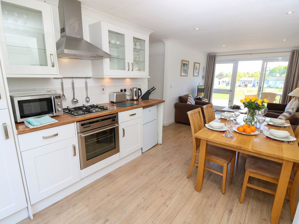 A kitchen and dining area with a wooden dining table set for four and a sitting area with a TV at Cape 14 in Yarmouth