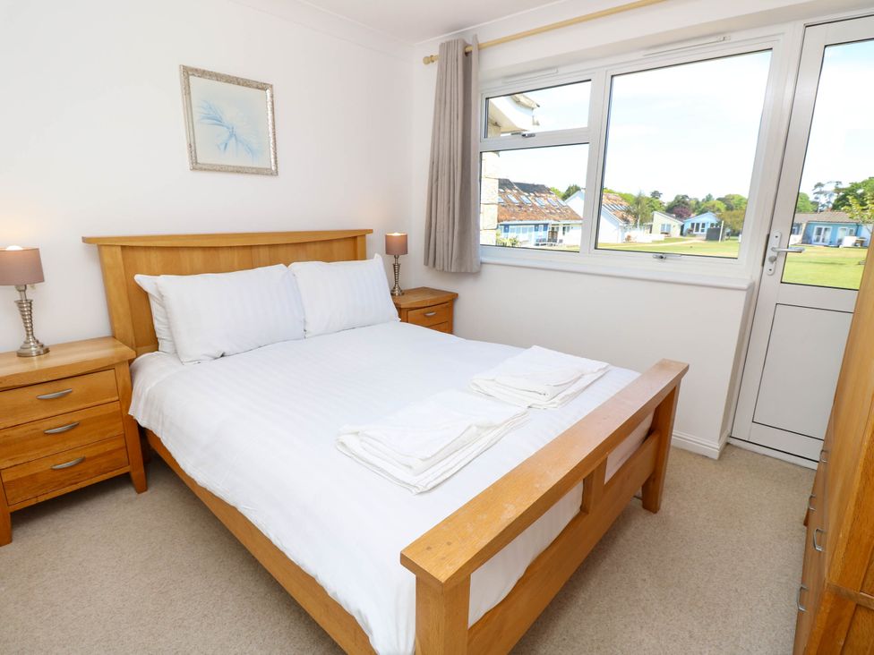 A bedroom with a wooden double bed white bedding two bedside tables with lamps a window and a door at Cape 14 in Yarmouth
