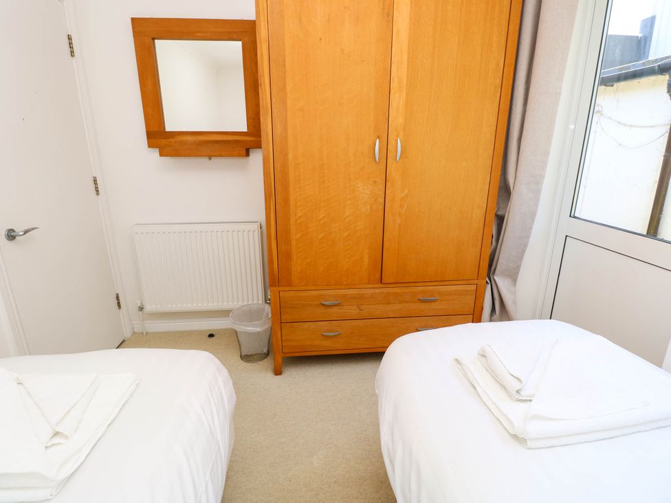 A bedroom with two beds with folded towels on them a wooden wardrobe a wall mirror a radiator and a window at Cape 14 Yarmouth