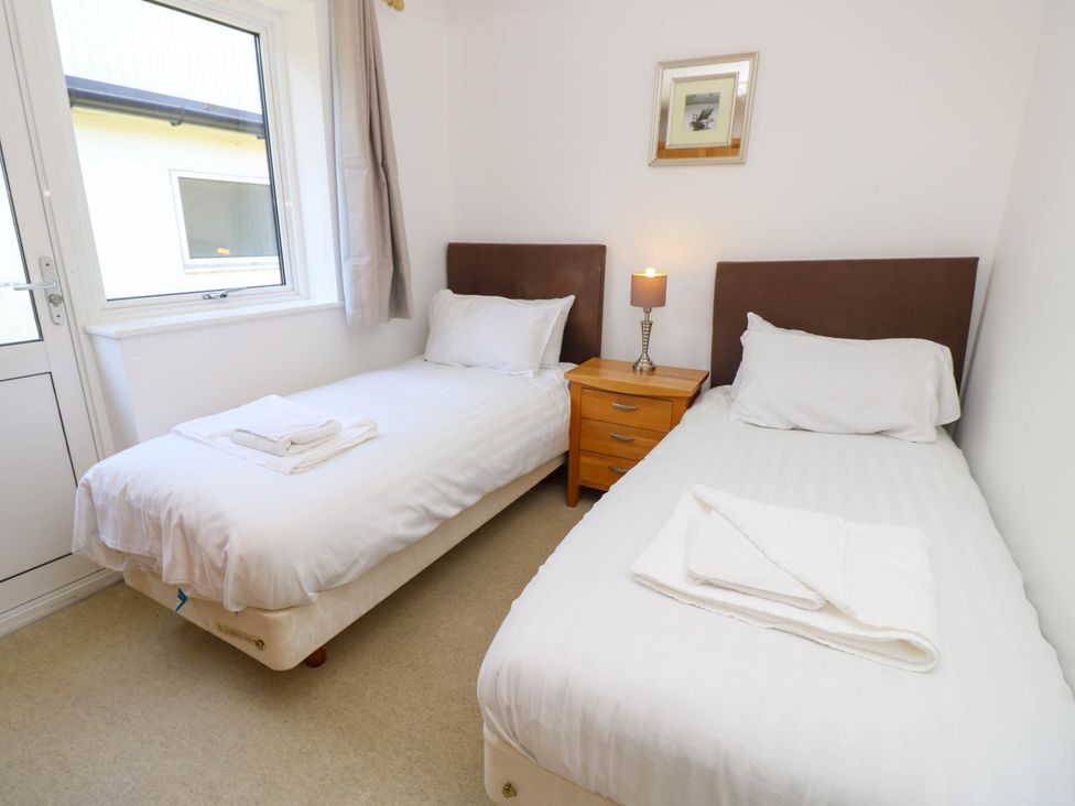 A bedroom with two single beds with white linens a wooden nightstand and a lamp between at Cape 14 in Yarmouth
