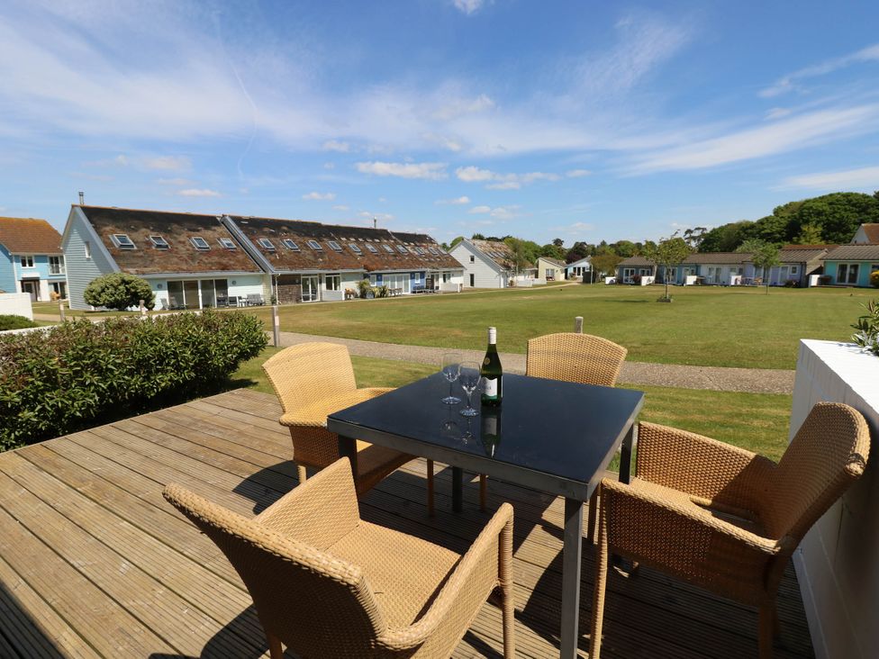 An outdoor patio with a black table and four wicker chairs overlooking a grassy area with row houses at Cape 14 in Yarmouth
