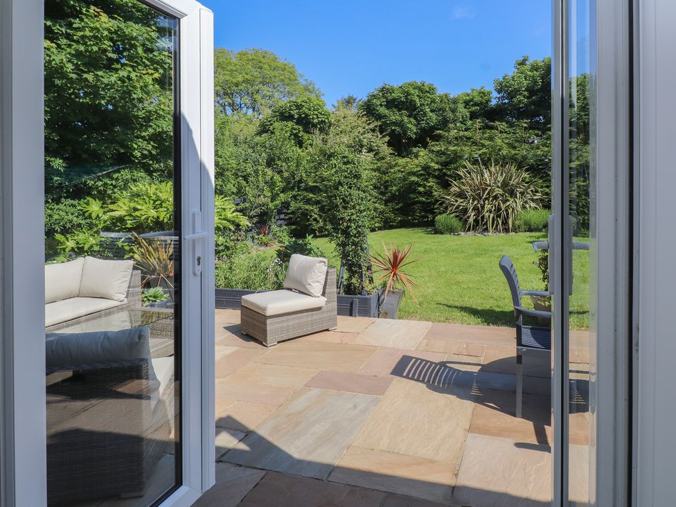 A patio with outdoor chairs and a table opening onto a garden with grass and trees at Annexe at Ty Moel Isaf in Pengorffwysfa near Amlwch