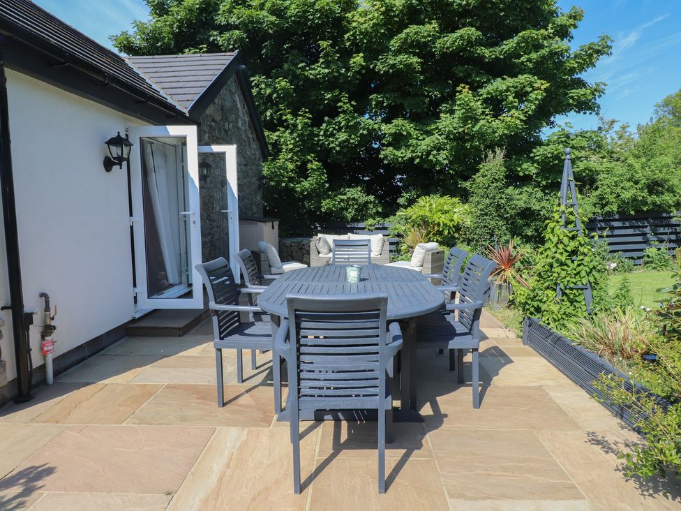 A patio with a table and eight chairs next to a white house and garden at Annexe at Ty Moel Isaf in Pengorffwysfa near Amlwch