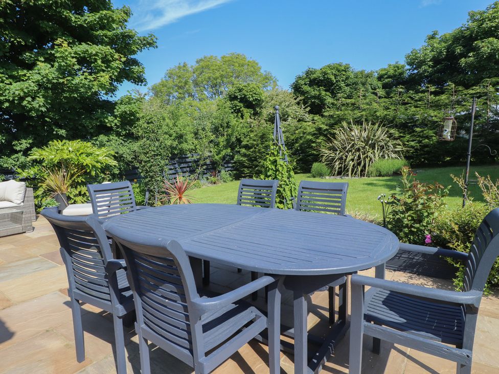An outdoor patio with a blue table and six chairs surrounded by grass and plants at Annexe at Ty Moel Isaf in Pengorffwysfa near Amlwch