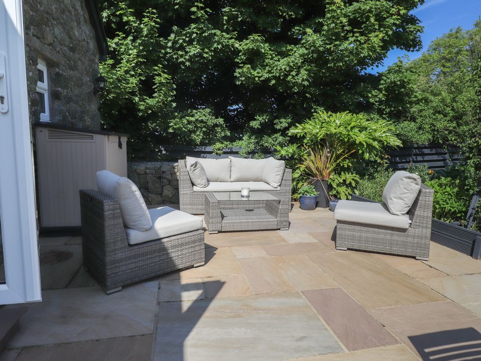 An outdoor patio with wicker chairs a wicker sofa and a wicker coffee table surrounded by plants at Annexe at Ty Moel Isaf in Pengorffwysfa near Amlwch