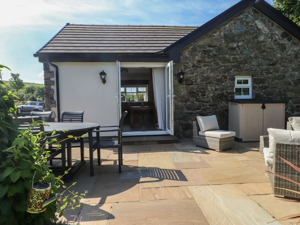 An outdoor patio with table and chairs and wicker seating in front of a building with stone and white walls at Annexe at Ty Moel Isaf in Pengorffwysfa near Amlwch