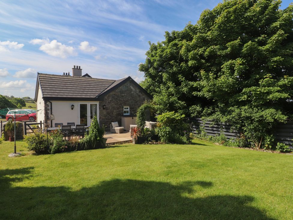 A house with a stone wall and patio chairs in a garden with a lawn and large trees at Annexe at Ty Moel Isaf Pengorffwysfa near Amlwch