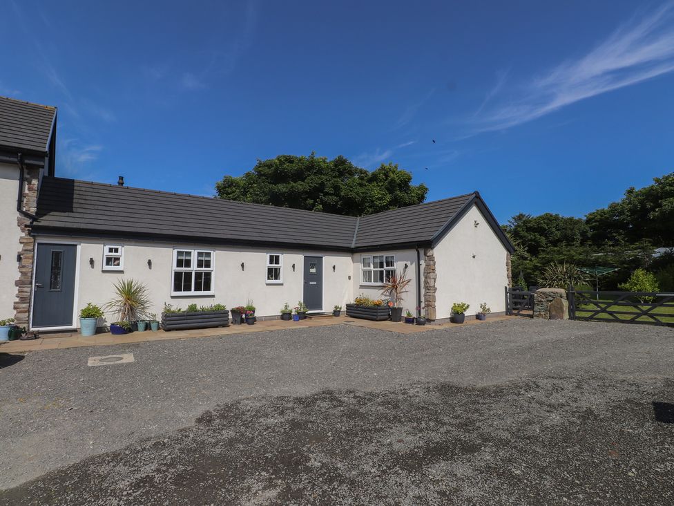 A white single-story house with gray doors and windows surrounded by potted plants and gravel driveway at Annexe at Ty Moel Isaf in Pengorffwysfa near Amlwch