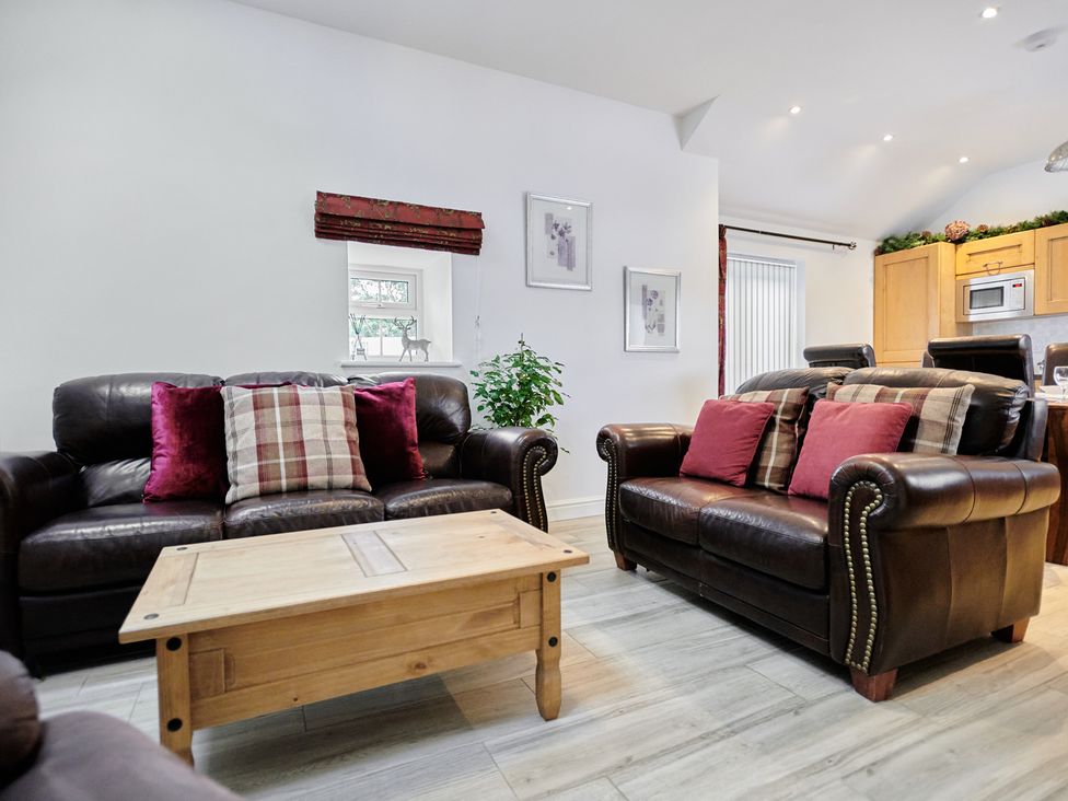 A living room with two brown leather sofas red and plaid cushions a wooden coffee table and kitchen cabinets at Annexe at Ty Moel Isaf in Pengorffwysfa near Amlwch