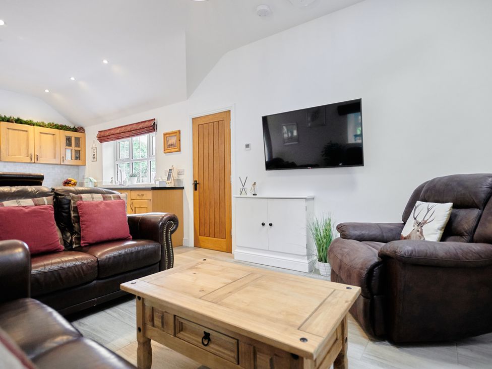 A living room with brown leather sofas a wooden coffee table a wall-mounted TV and a kitchen area at Annexe at Ty Moel Isaf in Pengorffwysfa near Amlwch
