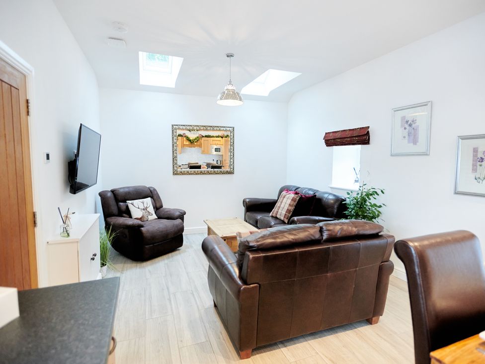 A living room with brown leather sofas a wooden coffee table a flat screen tv on the wall and skylights at Annexe at Ty Moel Isaf in Pengorffwysfa near Amlwch