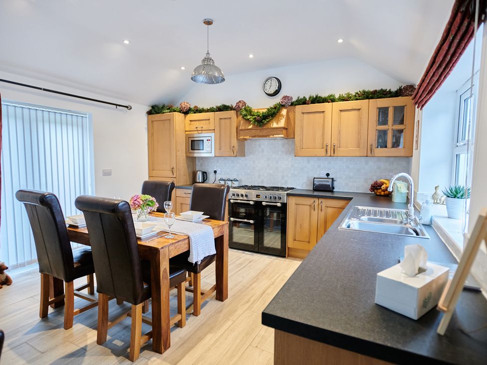 A kitchen with wooden cabinets a dining table with four chairs and a sink at Annexe at Ty Moel Isaf in Pengorffwysfa near Amlwch