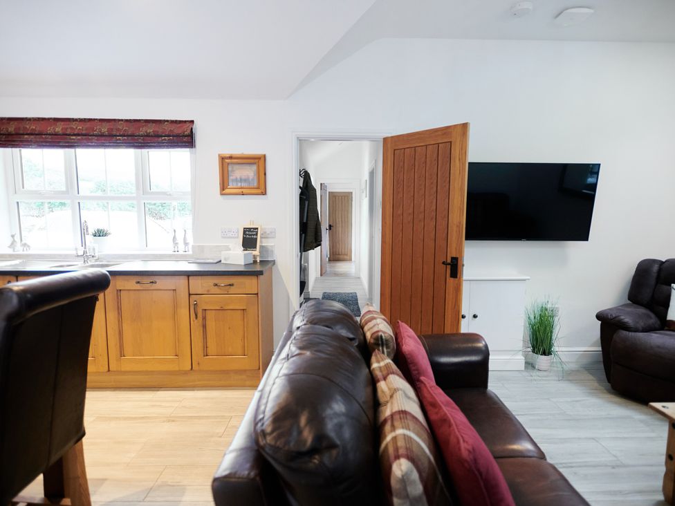 A living room with a leather sofa and cushions a wooden door and a wall-mounted TV at Annexe at Ty Moel Isaf in Pengorffwysfa near Amlwch