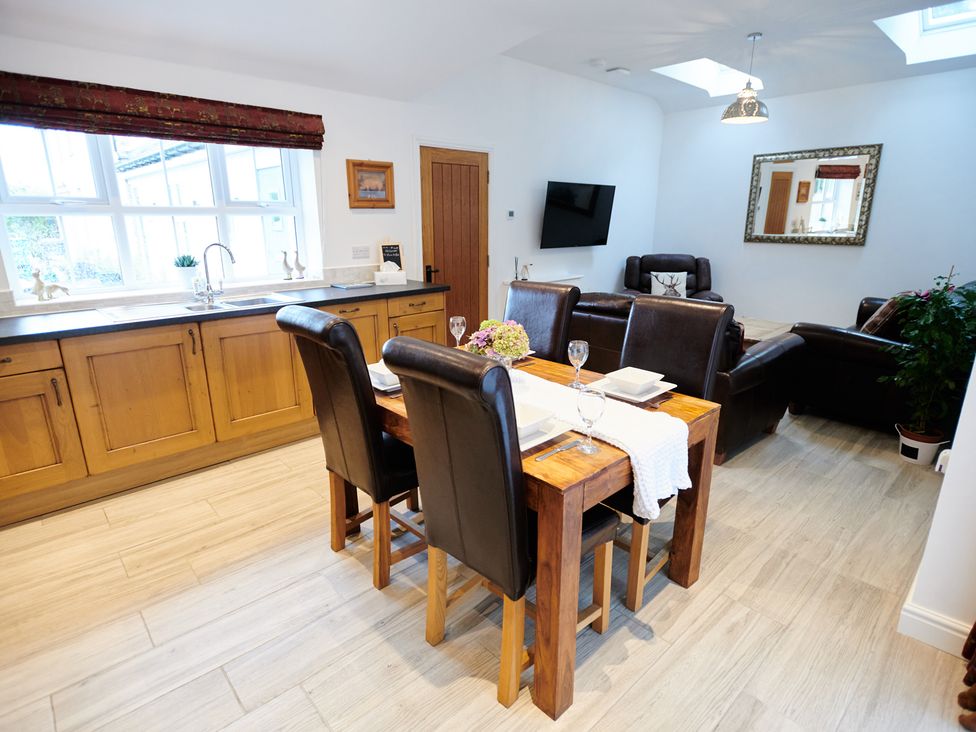 A combined kitchen and living area with wooden cabinets a dining table with four chairs and leather sofas at Annexe at Ty Moel Isaf Pengorffwysfa near Amlwch
