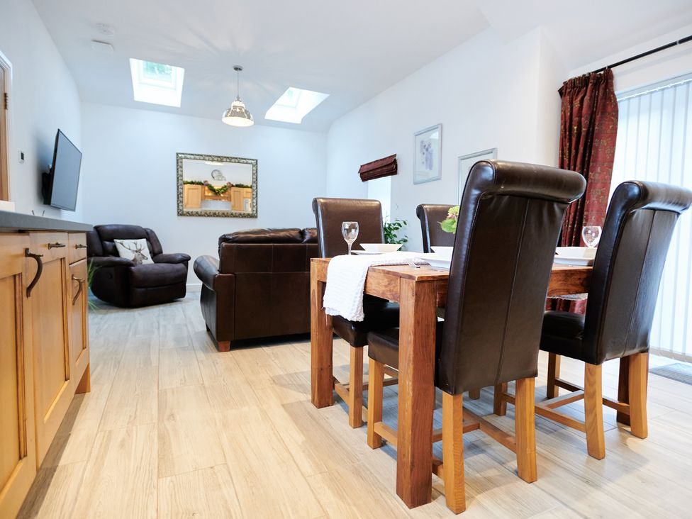 A dining area with a wooden table and leather chairs next to a seating area with leather sofas and armchair at Annexe at Ty Moel Isaf in Pengorffwysfa near Amlwch