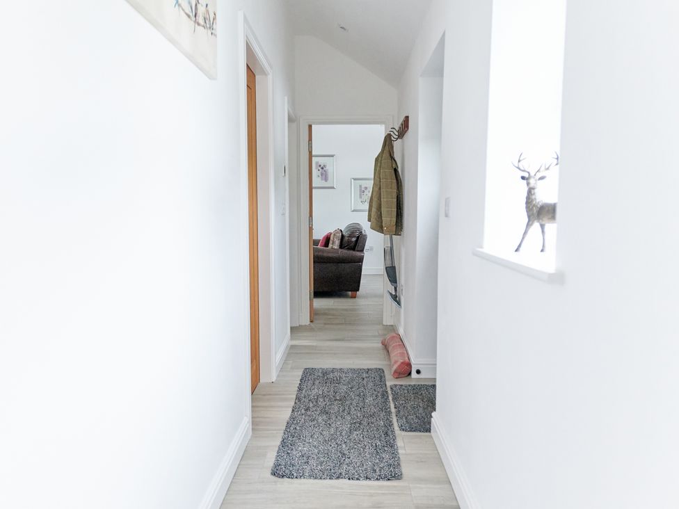 A hallway with rugs on the floor a coat hanging on the wall and a figure of a deer in a window at Annexe at Ty Moel Isaf in Pengorffwysfa near Amlwch