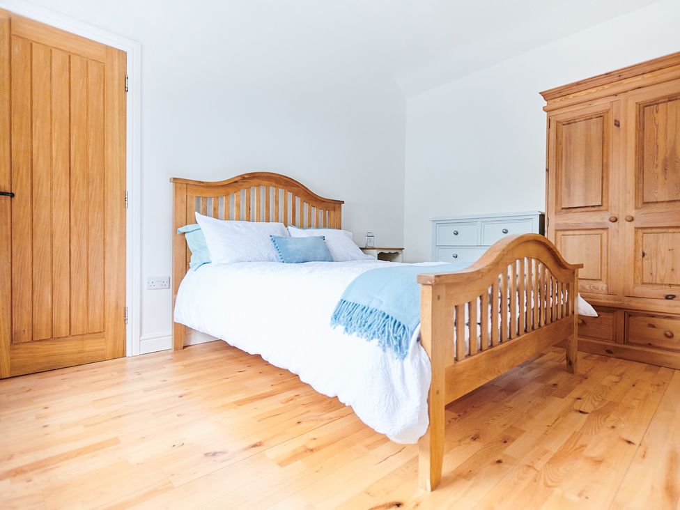 A bedroom with a wooden bed frame white bedding blue pillows a wooden wardrobe and a blue chest of drawers at Annexe at Ty Moel Isaf Pengorffwysfa near Amlwch