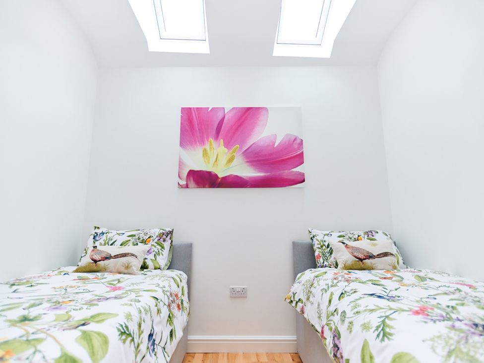 A bedroom with two single beds floral bedding and a flower painting on the wall at Annexe at Ty Moel Isaf in Pengorffwysfa near Amlwch