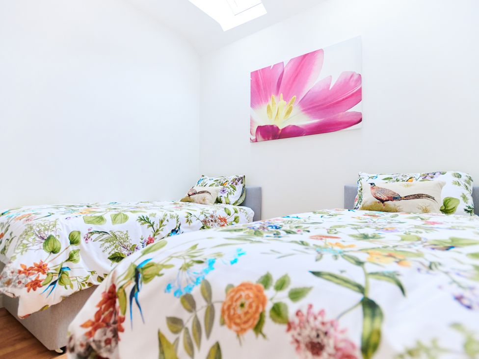 A bedroom with two single beds with floral bedding and a large pink flower artwork on the wall at Annexe at Ty Moel Isaf in Pengorffwysfa near Amlwch