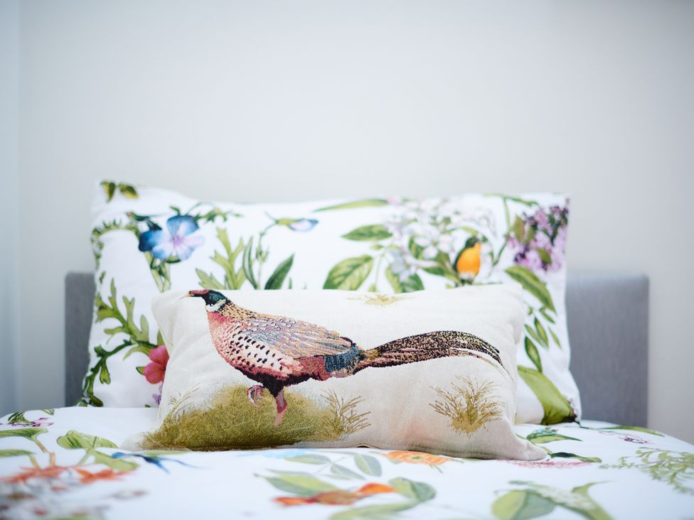 A bed with floral sheets and pillows including a decorative pillow with a bird design at Annexe at Ty Moel Isaf in Pengorffwysfa near Amlwch
