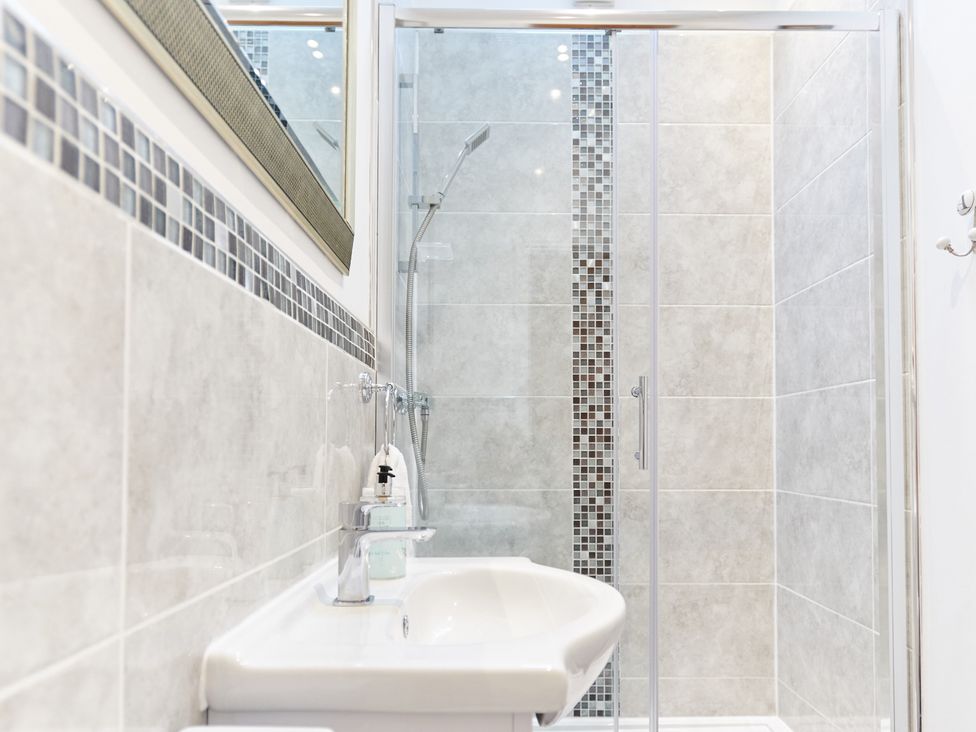 A bathroom with a sink and a glass-enclosed shower with tiled walls and mosaic tile accents at Annexe at Ty Moel Isaf in Pengorffwysfa near Amlwch