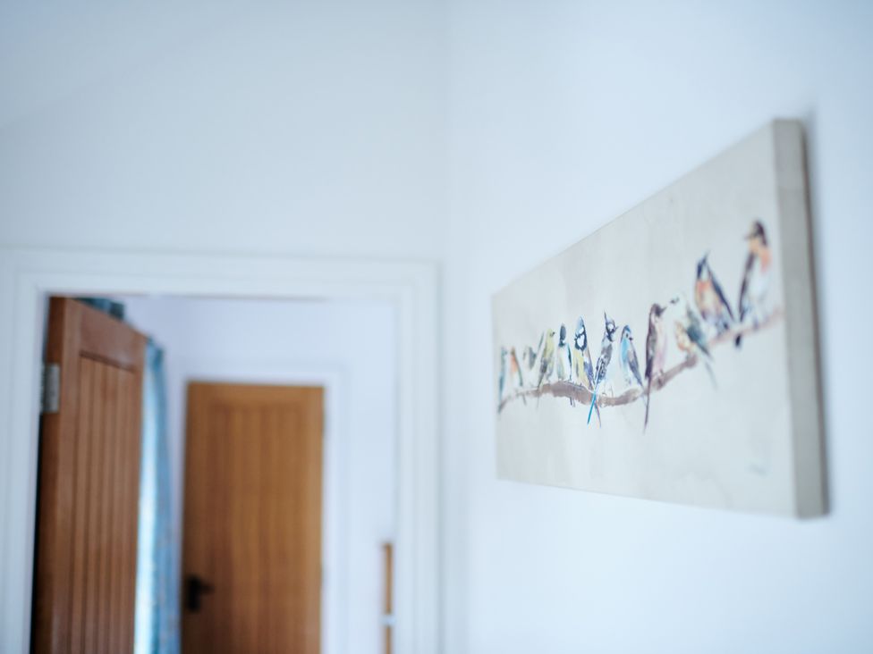 A white wall with a colorful painting of birds on a branch and wooden doors in the background at Annexe at Ty Moel Isaf in Pengorffwysfa near Amlwch