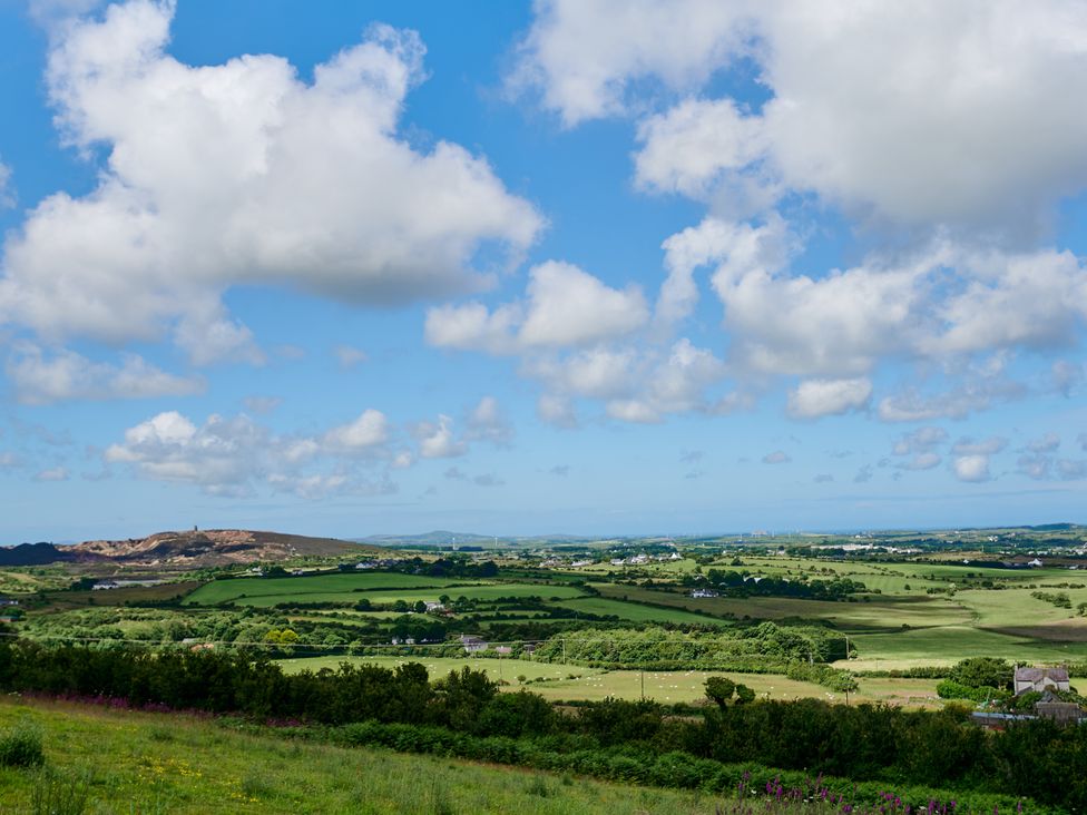 A countryside landscape with fields trees houses and hills under a partly cloudy sky at Annexe at Ty Moel Isaf in Pengorffwysfa near Amlwch