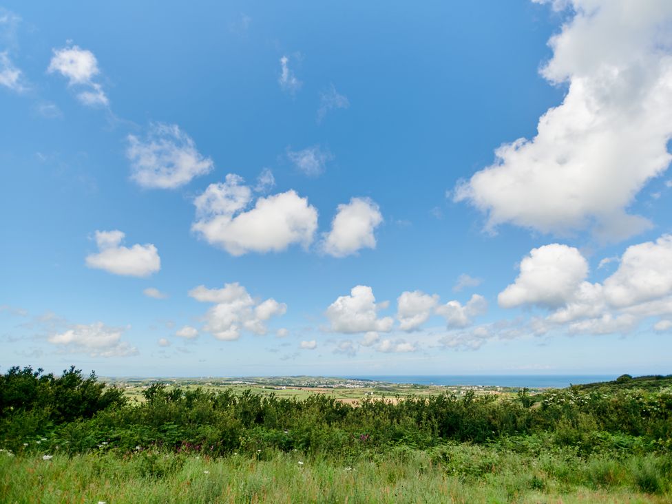 A landscape view of green fields bushes and a distant coastline under a blue sky with clouds at Annexe at Ty Moel Isaf in Pengorffwysfa near Amlwch