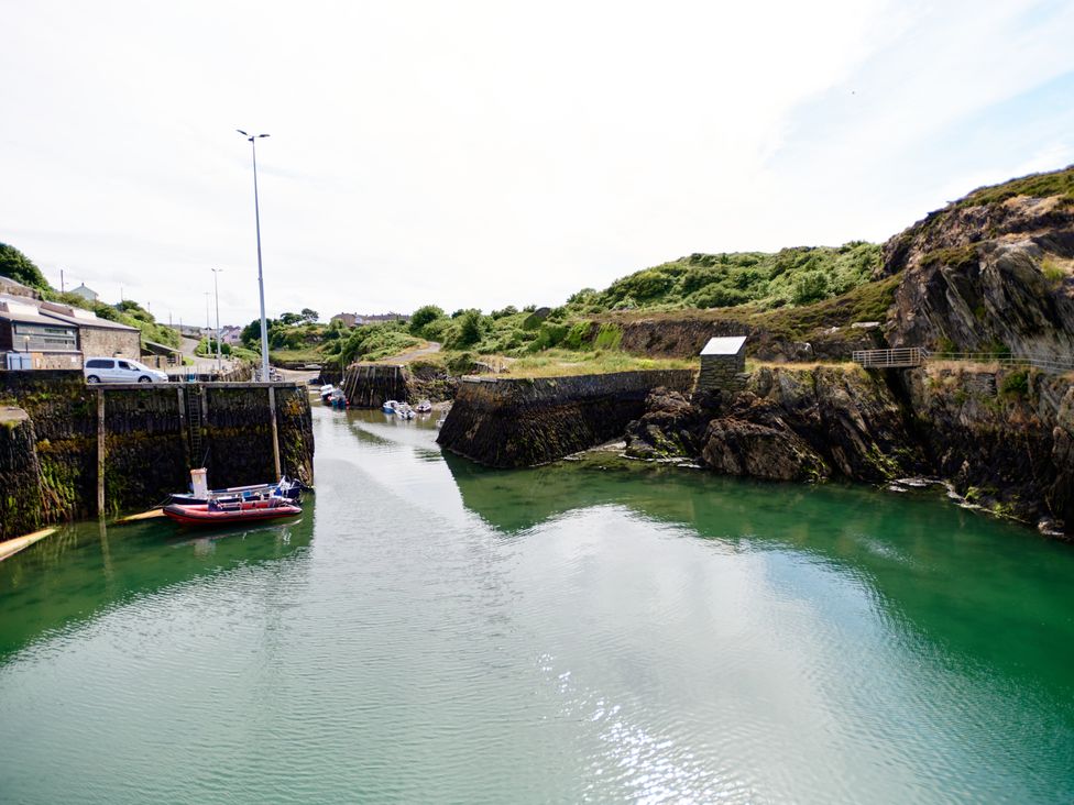 A small harbor with boats moored alongside stone piers and green hills in the background at Annexe at Ty Moel Isaf in Pengorffwysfa near Amlwch