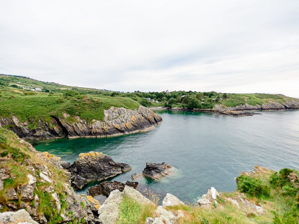 A coastal landscape with rocky cliffs and green vegetation overlooking a calm bay at Annexe at Ty Moel Isaf in Pengorffwysfa near Amlwch