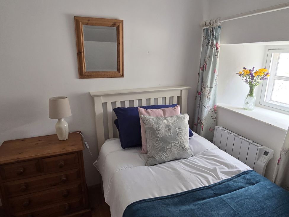 A bedroom with a bed, lamp, dresser, and flowers at Picket Mead Southleigh near Colyton