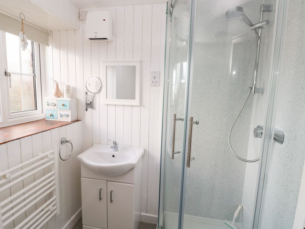 A bathroom with a shower, sink, and storage at 8 Rogeston Cottages Haverfordwest