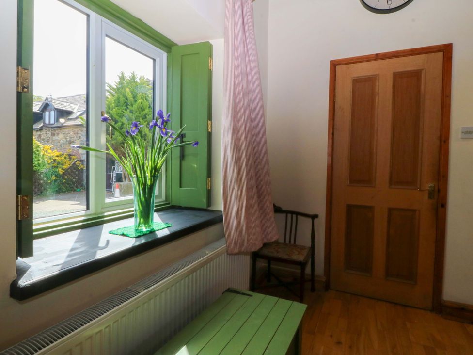 A hallway with a window, flowers, chair and door at Pen Glorian in Conwy