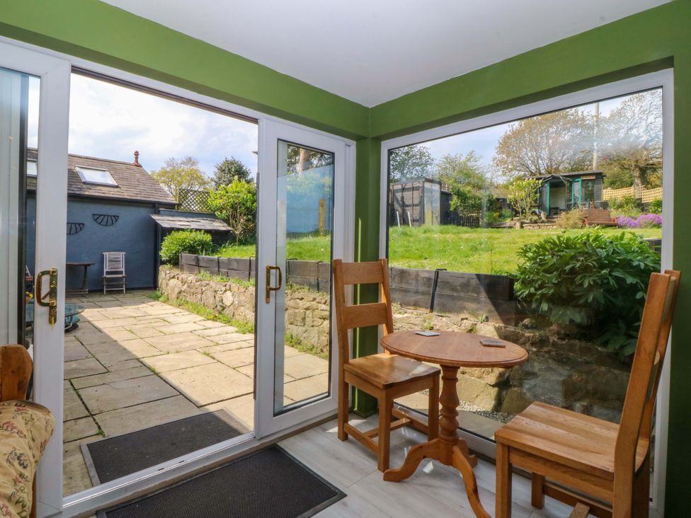 A conservatory with two chairs and a table overlooking a garden at Pen Glorian in Conwy