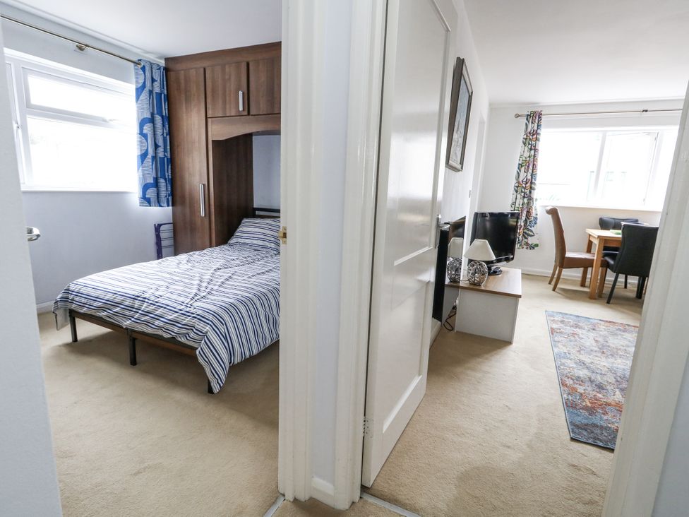 A bedroom with a bed and a doorway leading to a living area at Beachcombers, 13 Chesil House in Bridport