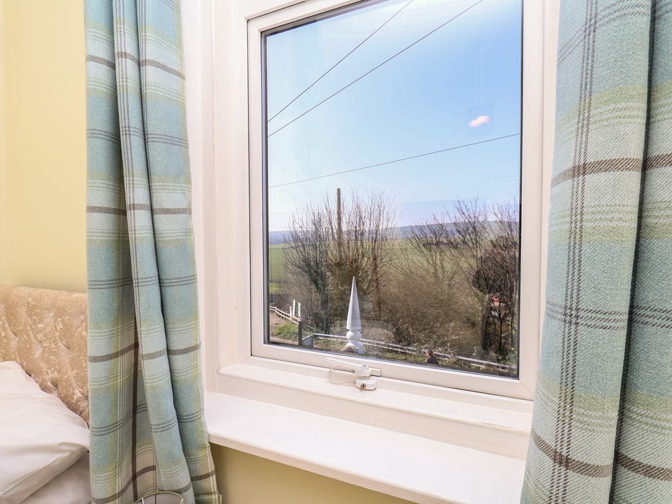 A bedroom window with curtains and view of trees at Kingfisher House in Staithes