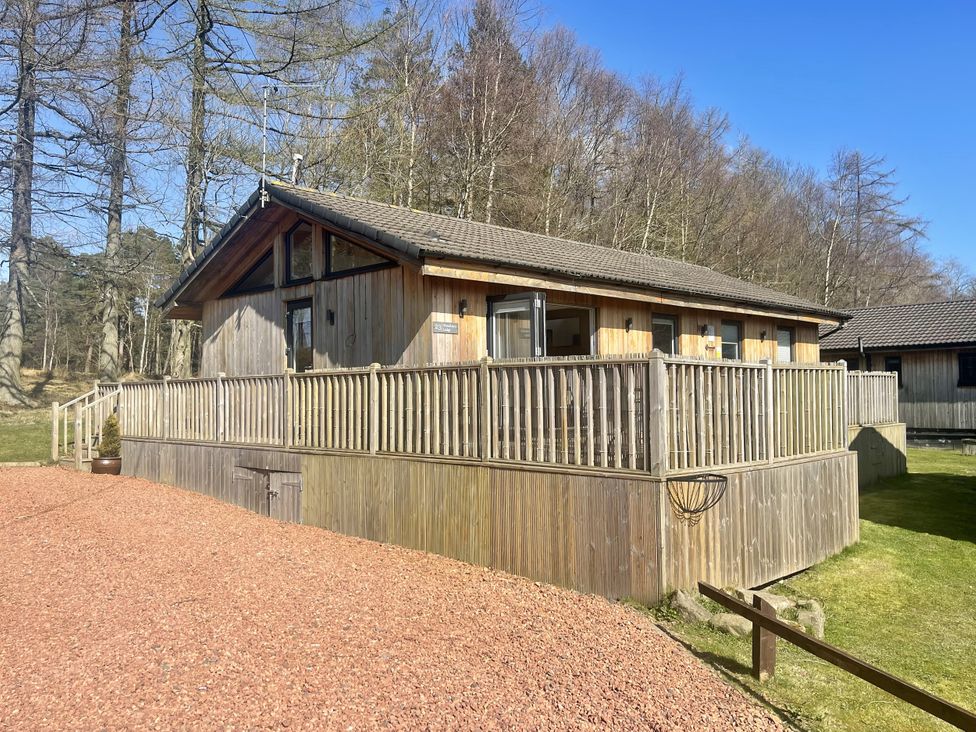 A wooden house with decking and gravel driveway at Woodburn Lodge Otterburn