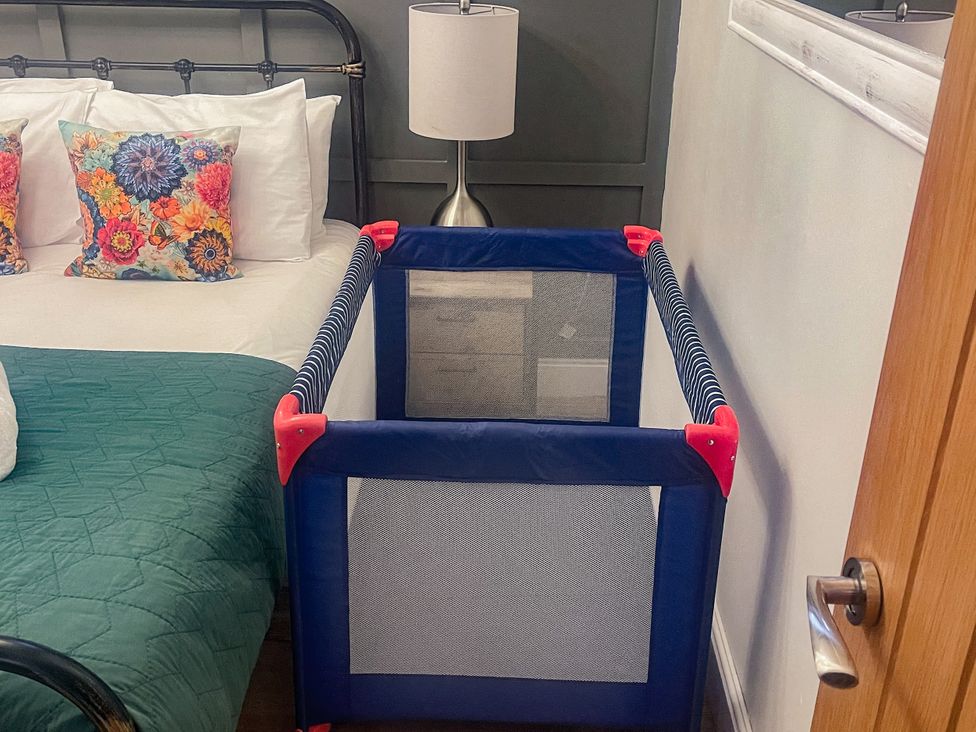 A bedroom with a crib beside a bed at Woodburn Lodge in Otterburn