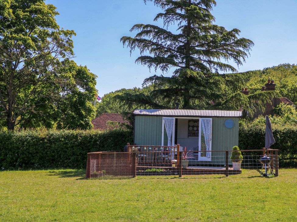 A small garden shed with open doors and a fenced grassy yard surrounded by trees at Songbirds in St Michaels Kent